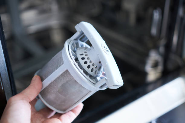 Hand holding a washing machine filter, demonstrating its removal for cleaning purposes.